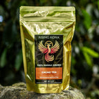 Gold tea package with a logo on a rock in front of green foliage
